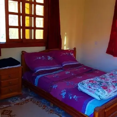 a bedroom with a bed with purple sheets and a window at Hotel Boutaghrar in Kalaat MGouna