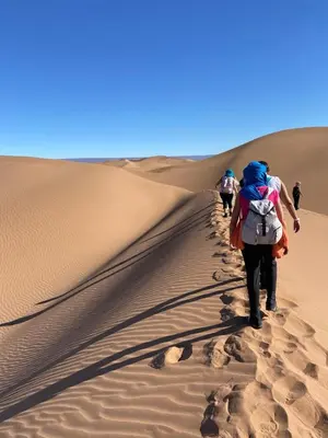 people walking down a sand dune in the desert at Bivouac Le secret des dunes, lac Iriqui in Foum Zguid