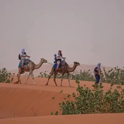 two people are riding on camels in the desert at Sahara pathfinders in Mhamid