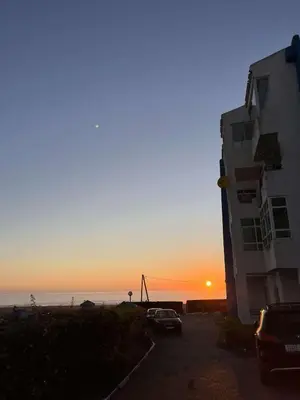 a sunset at the beach with a building and cars at Sublime appartement front de mer in Oulad Akkou