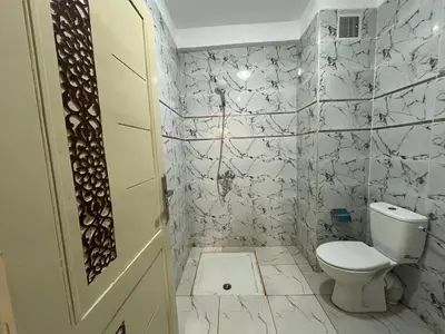 a bathroom with a toilet and a white tiled wall at Saha khedra in Oulad Akkou