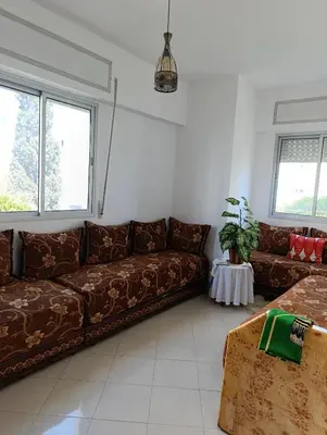 a living room with a brown couch and two windows at Appartement martil in Oulad Akkou