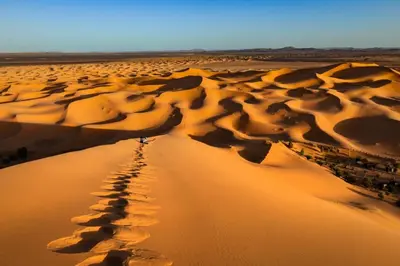 a person walking across a desert with footprints in the sand at Camp fire Dreams in Merzouga