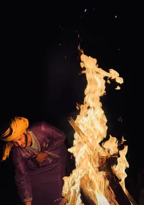 a woman is standing next to a large fire at Merzouga in Oulad Akkou