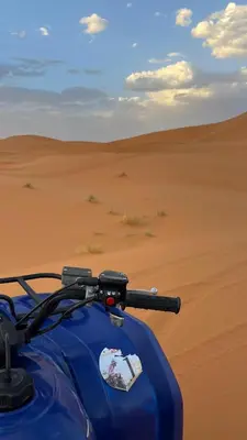 a blue motorcycle parked in the desert at Merzouga in Oulad Akkou