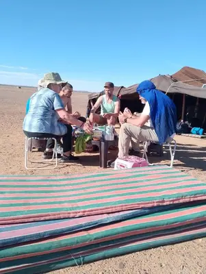 a group of people sitting around a table on the beach at Emosion desert trekking in Hassilabied