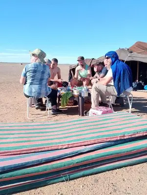 a group of people sitting at a table on the beach at Emosion desert trekking in Hassilabied
