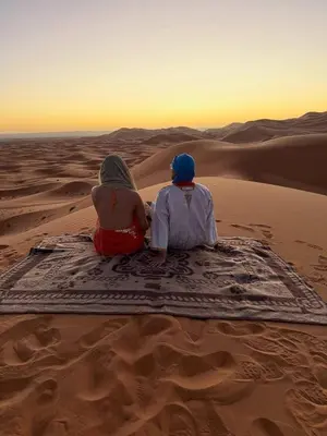 two people sitting on a rug in the desert at Glamping Under Stars in Merzouga