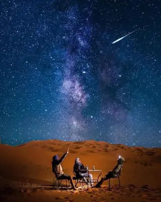 a group of three people sitting at a table under the stars at Glamping Under Stars in Merzouga