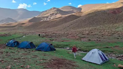 a woman walking in front of three tents in a mountain at Gite d'étape La terre Amazigh in Oulad Akkou