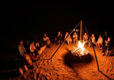 a group of people sitting around a fire at night at Bedouin House in Merzouga