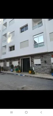 a large white building with windows on a street at Appartement à côté la plage in Oulad Akkou