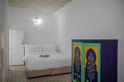 a bedroom with a white bed and a colorful cabinet at Dar Mohamadia in Fès