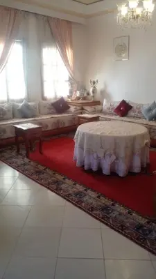 a living room with a table and a red rug at Cosy villa in Oulad Akkou