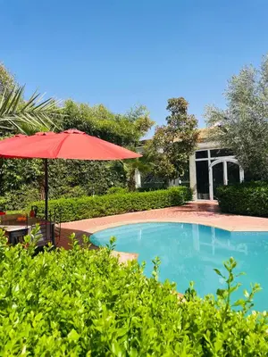 a swimming pool with a red umbrella and a house at Villa MSHolidays 3 palmiers avec piscine marrakech in Marrakech