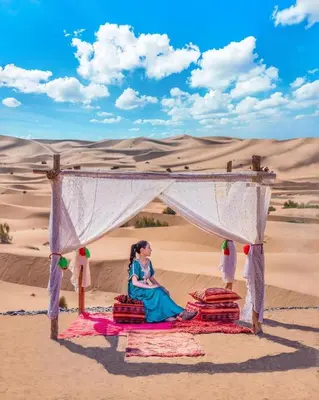 a woman sitting under a tent in the desert at Merzouga Luxurious Stay in Merzouga