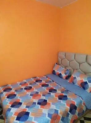a bed in a bedroom with an orange wall at Studio meublé calme in Oulad Akkou