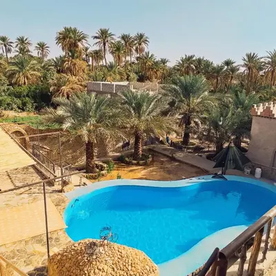 a large blue swimming pool with palm trees in the background at Riad IZRAREN in FIGUIG in Zenaga