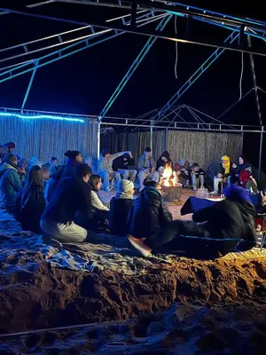 a group of people sitting around a fire in a tent at Desert Hassi labiad Camp in Merzouga