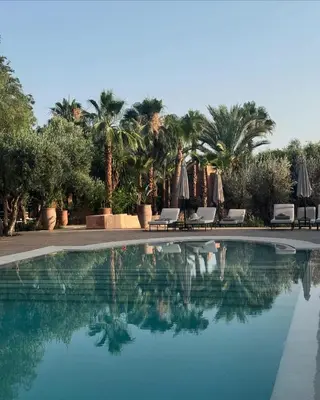 a swimming pool with chairs and umbrellas and palm trees at Le mas de l'Ourika, maison d'hôtes in Aït Zat