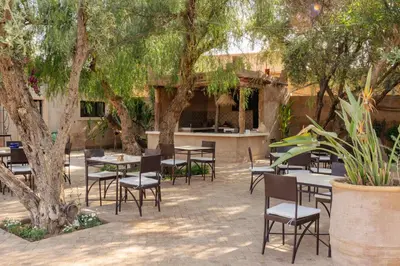 an outdoor patio with tables and chairs under trees at Le mas de l'Ourika, maison d'hôtes in Aït Zat