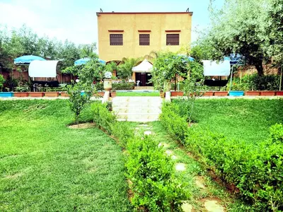 a garden with trees and a building in the background at Hotel&Restaurant Atlas Symphony in Ourika
