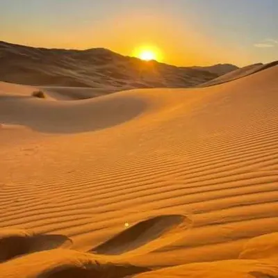 a desert with the sun setting in the horizon at Desert Campo in Oulad Akkou