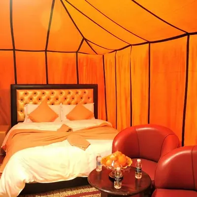 a bed in a tent with two chairs and a table at Desert Bloom Luxury Camp in Merzouga