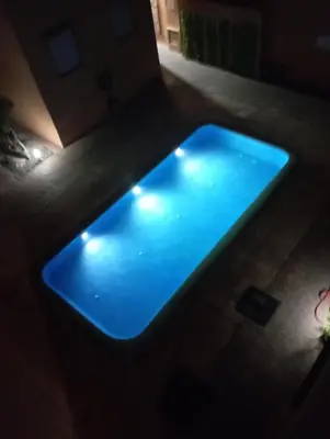 a blue swimming pool in a dark room with lights at Appartement Nour sakane targa kech in Oulad Akkou