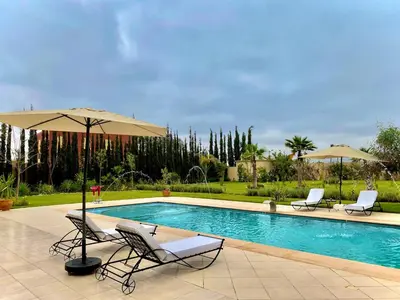 a swimming pool with two chairs and an umbrella at Villa Rania Le luxe à Marrakech in Ourika