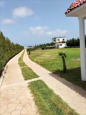 a dirt road next to a field with a house at Villa piscine espace vert luxueuse in Oulad Akkou
