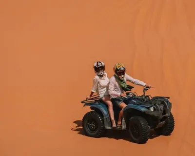 two people riding on a quad bike in the sand at Nourland Luxury Camp in Merzouga