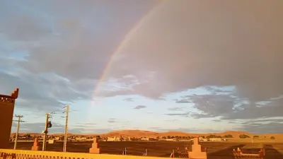 a rainbow is in the sky over a field at Villasaharamerzouga in Merzouga