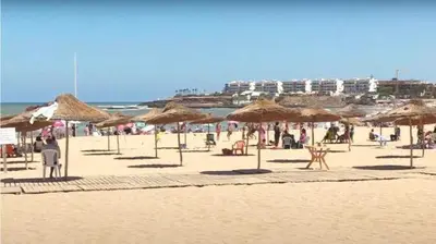 a beach with many straw umbrellas and people on it at La siesta beach resort in Oulad Akkou