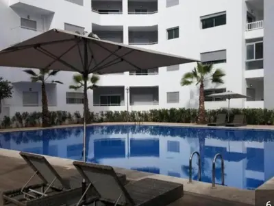 a pool with two chairs and an umbrella next to a building at La siesta beach resort in Oulad Akkou