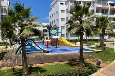 a playground with a slide in a park with palm trees at La siesta beach resort in Oulad Akkou
