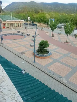 a plaza with a fountain and trees and a building at Hôtel des cedres azrou in Oulad Akkou