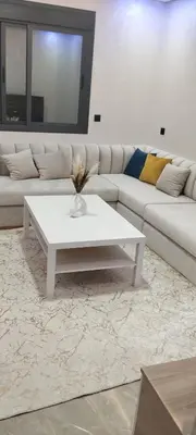 a living room with a white couch and a white coffee table at شقة مفروشة 3 غرف حمامين مطبخ وصالون in Oulad Akkou