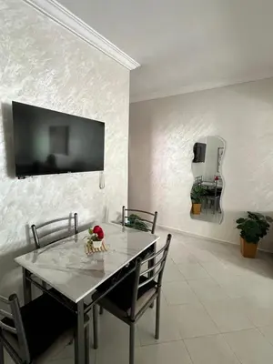 a dining room table with chairs and a tv on the wall at Diyar tanger in Oulad Akkou