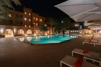 a swimming pool at night with chairs and a building at Amanar Hôtel & Spa Ouarzazate in Ouarzazate