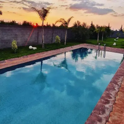 a large swimming pool with a sunset in the background at DAR MORAD VILLA AVEC PISCINE PRIVEE DANS UNE FERMe in Bou Azza