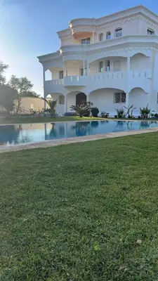 a large white building with a pool in front of it at Palm in Oulad Akkou