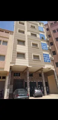 a large building with cars parked in front of it at Bousstan 1er in Oulad Akkou