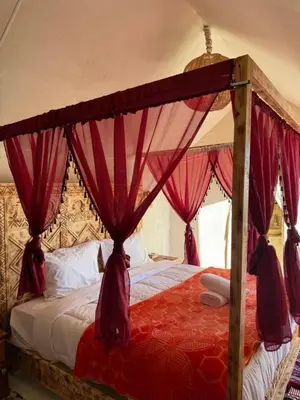 a bedroom with a canopy bed with red drapes at Desert luxury tents in Merzouga