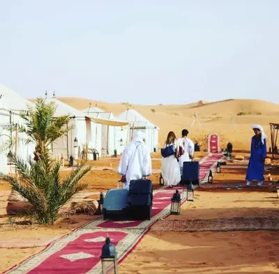 a group of people walking through the desert with luggage at Desert luxury tents in Merzouga