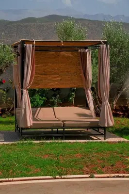 a bench with curtains on it in the grass at Maison blanche in Sbiti