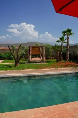 a swimming pool with a bench and palm trees at Maison blanche in Sbiti