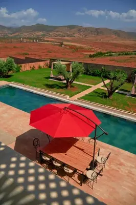 a red umbrella sitting on a table next to a pool at Maison blanche in Sbiti