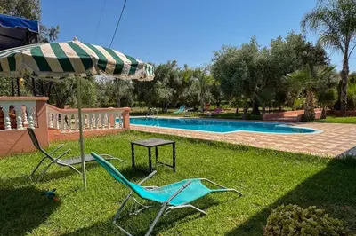 two chairs and an umbrella next to a swimming pool at Villa Jenane Rabia in Amezrou