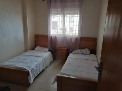 two beds in a small room with a window at Aicha's appartement 1 in Meknès
